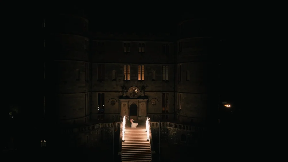 A couple dance on the stairs of Lulworth Castle in Dorset, with cold sparks framing them, filmed from the drone by spice wedding films