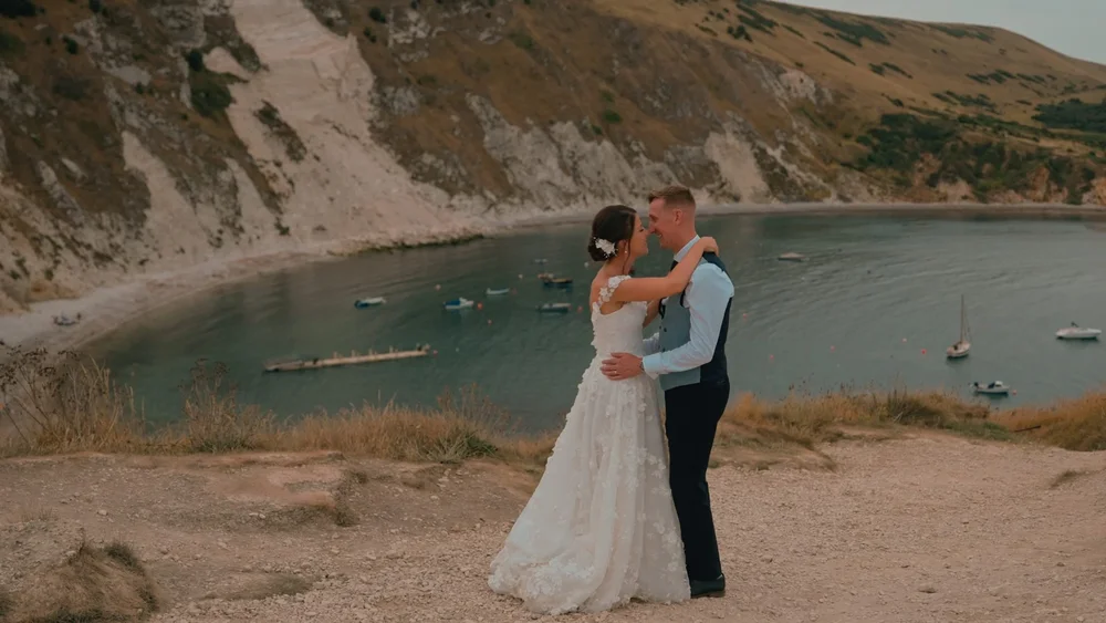 A wedding couple stand overlooking Lulworth Cove in Dorset while the sun sets, filmed by Spice Wedding Films
