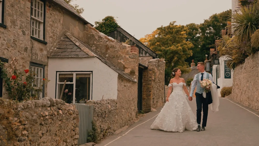 A wedding couple walk down the streets of Lulworth in Dorset, filmed by wedding videographer spice wedding films