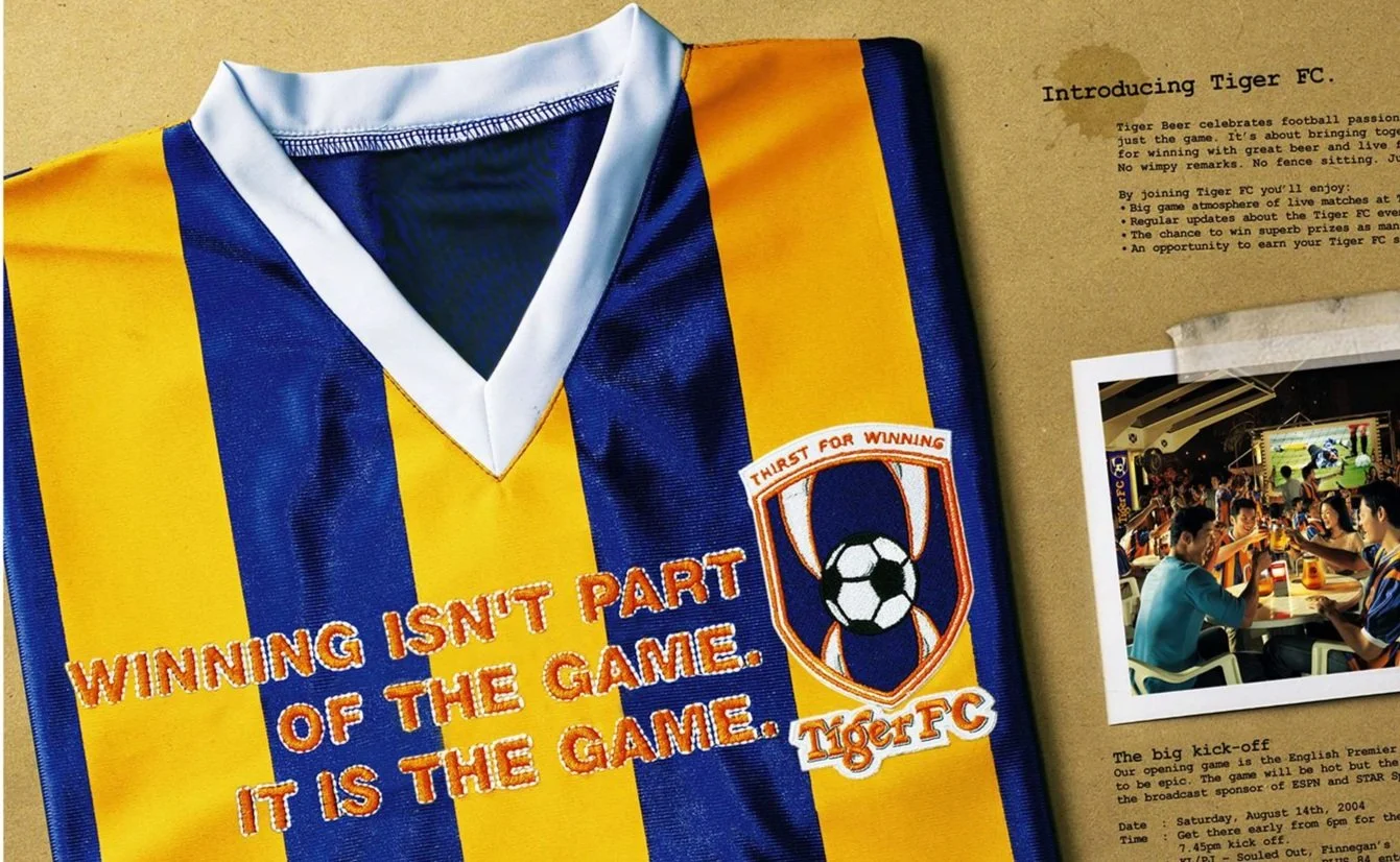 A blue and yellow striped soccer jersey with the words "Winning isn't part of the game. It is the game" embroidered on it, along with the Tiger FC logo.