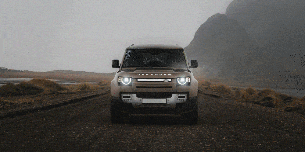 Front view of a silver Land Rover Defender driving on a dirt road in a remote, mountainous area