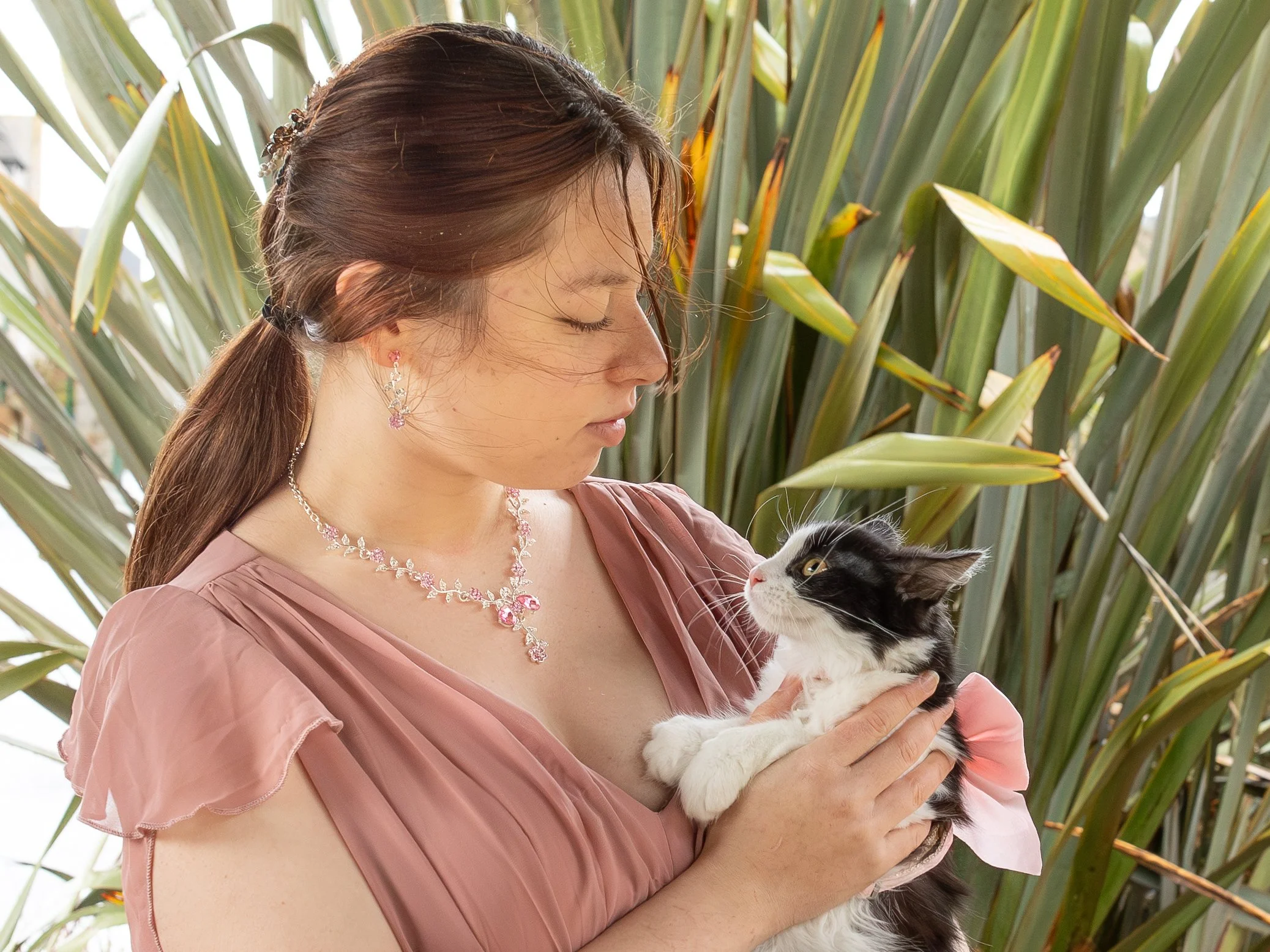 Une femme tenant un chat noir et blanc dans ses bras, avec de grandes plantes en arrière-plan.