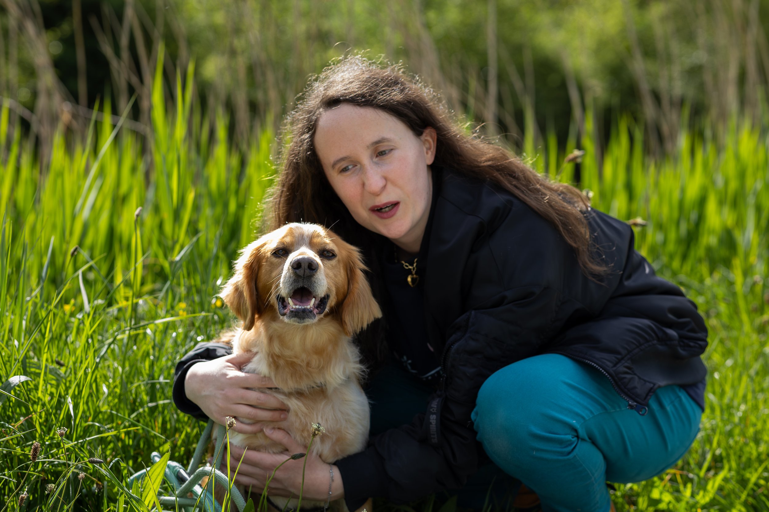 Une femme et un chien Golden Retriever dans un champ vert, la femme tient le chien près d'elle, tous deux semblent heureux et détendus.