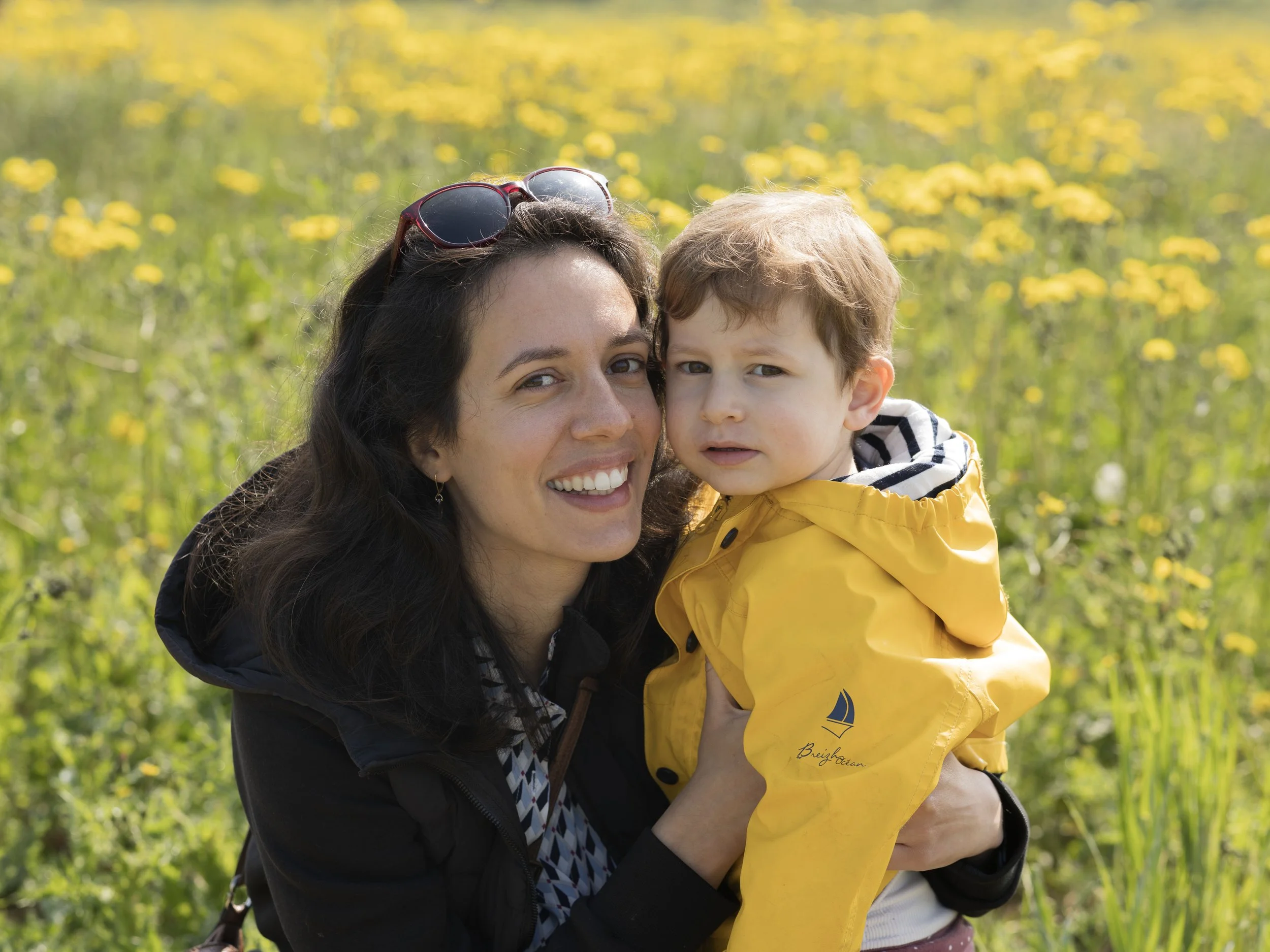 Une femme souriante tenant un jeune garçon dans un champ de fleurs jaunes.