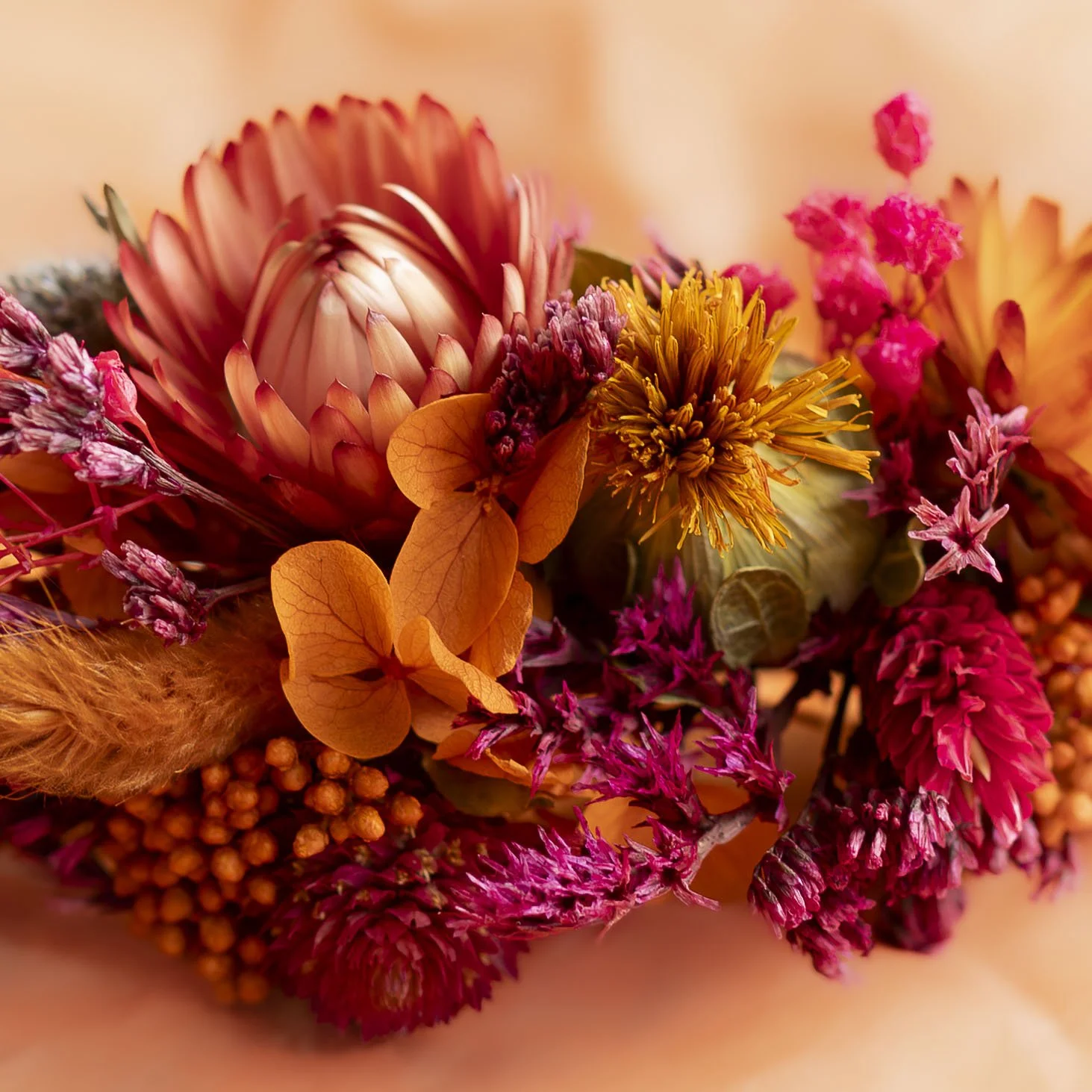 Une barrette de fleurs orangées préparé par Achillée et Sauvage destiné à la coiffure d'une mariée comprenant des proteas, des dracénas, des chrysanthèmes et autres fleurs dans les tons orange, rose et jaune.