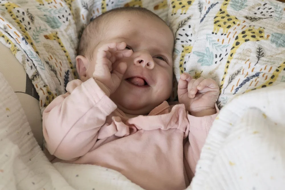 Un bébé souriant allongé dans un lit vêtu d'un pyjama rose.