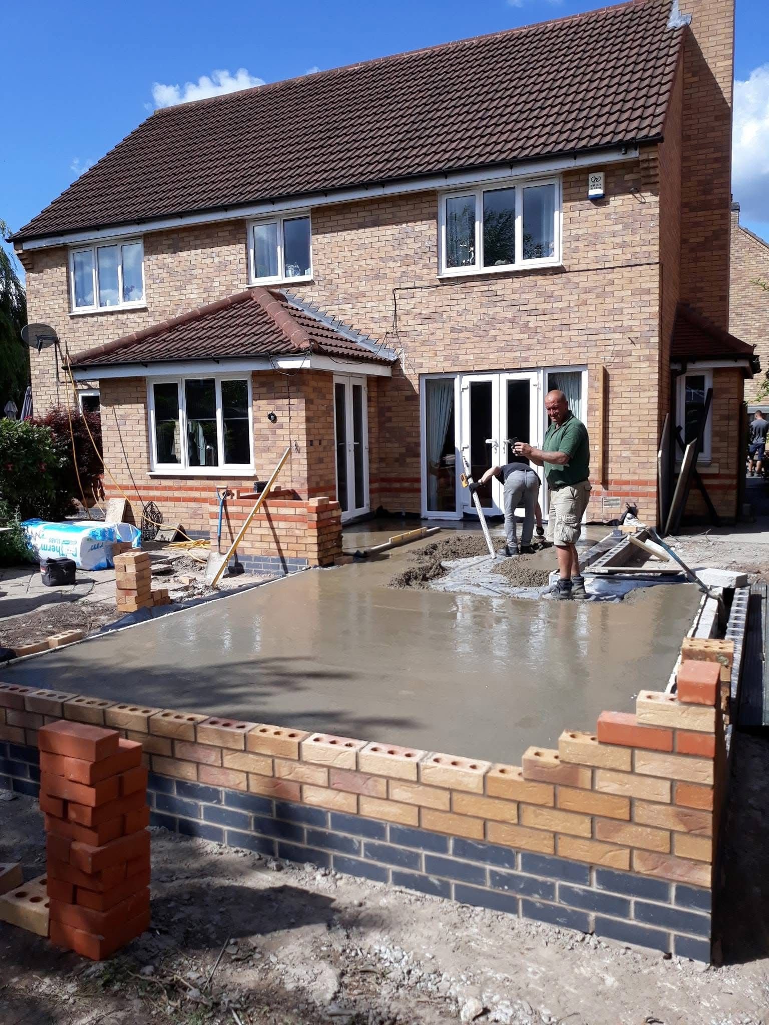 Construction workers laying a concrete foundation in front of a brick house.