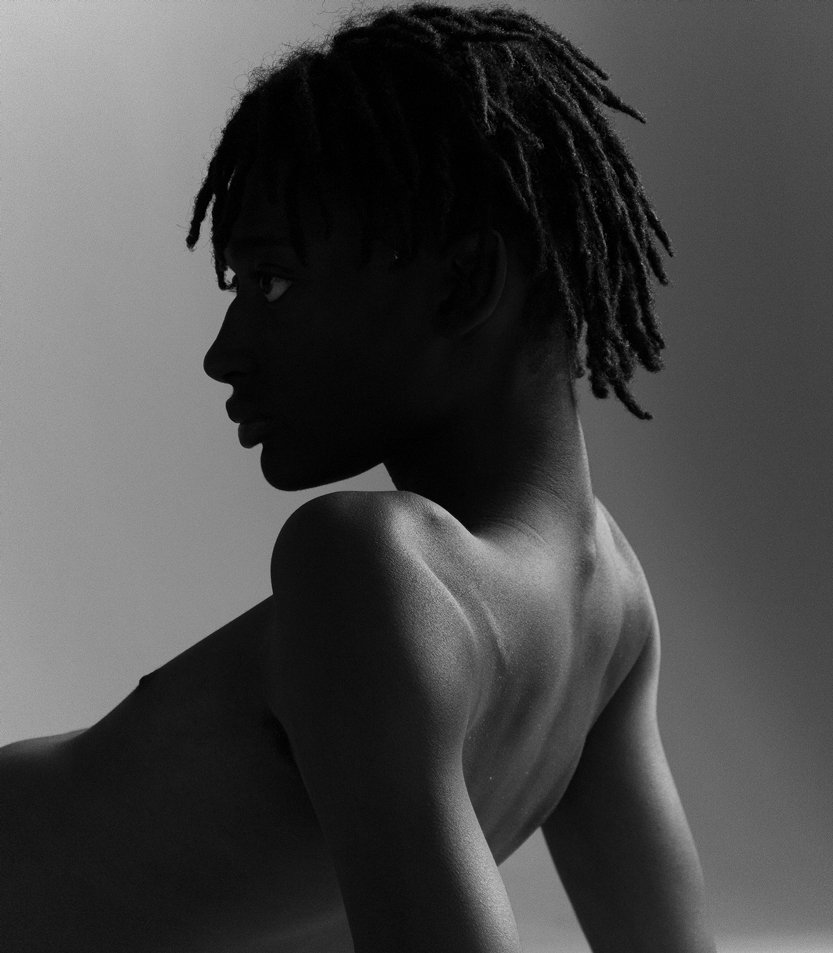 Black and white side profile of a shirtless person with dreadlocks, looking to the left.