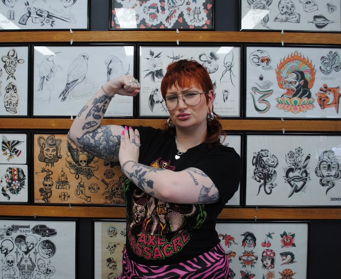 Needleslinger posing in front of tattoo flash