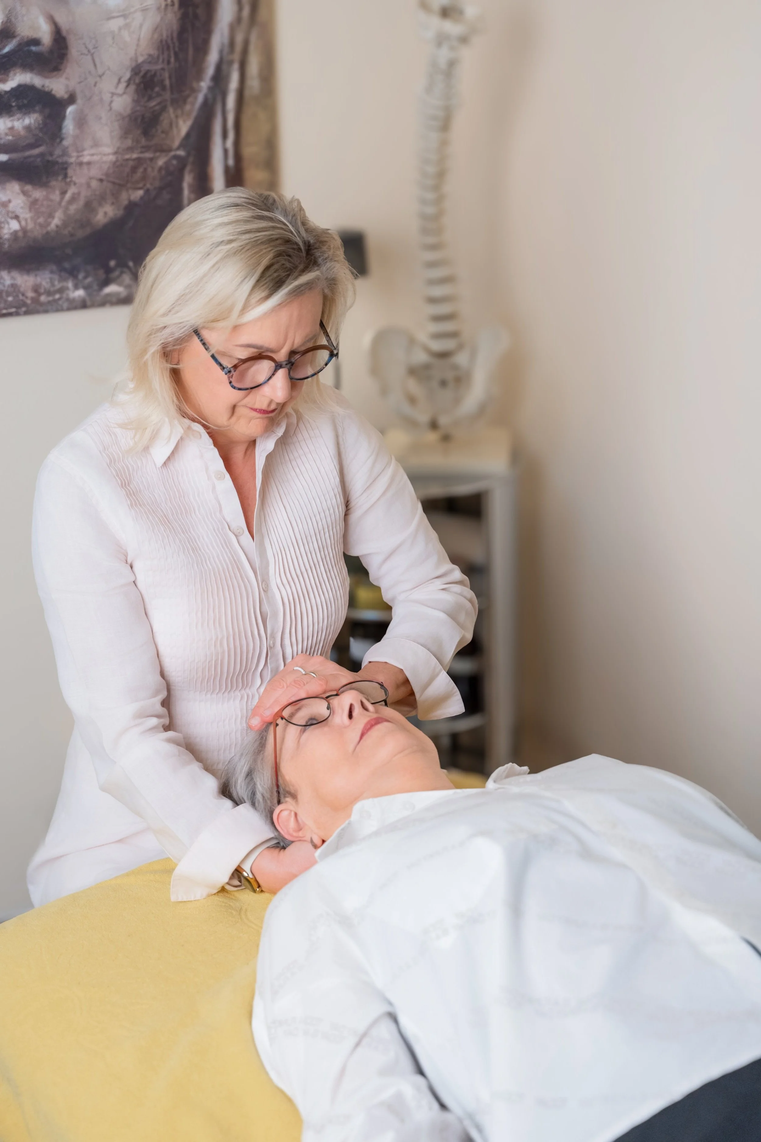 Therapeutin führt craniosacrale Therapie bei einem liegenden Patienten durch.