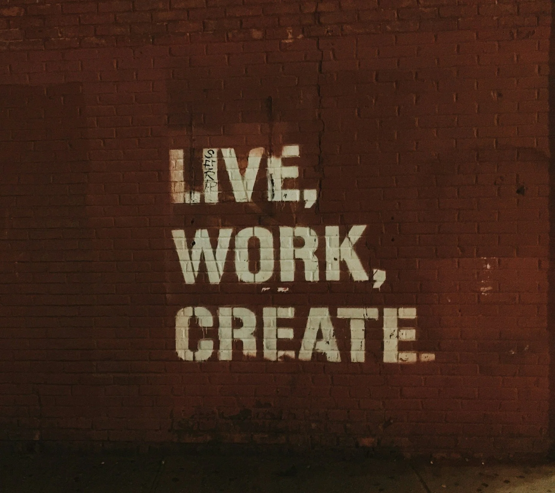 Brick wall with the words "LIVE, WORK, CREATE." stenciled in white paint.