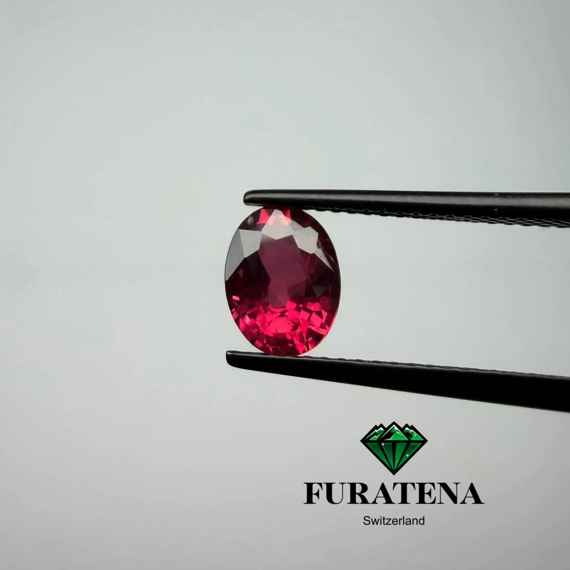 Une pierre précieuse rouge en forme de larme tenue par une pince, avec un logo en forme de diamant vert et le texte "FURATENA" en dessous.