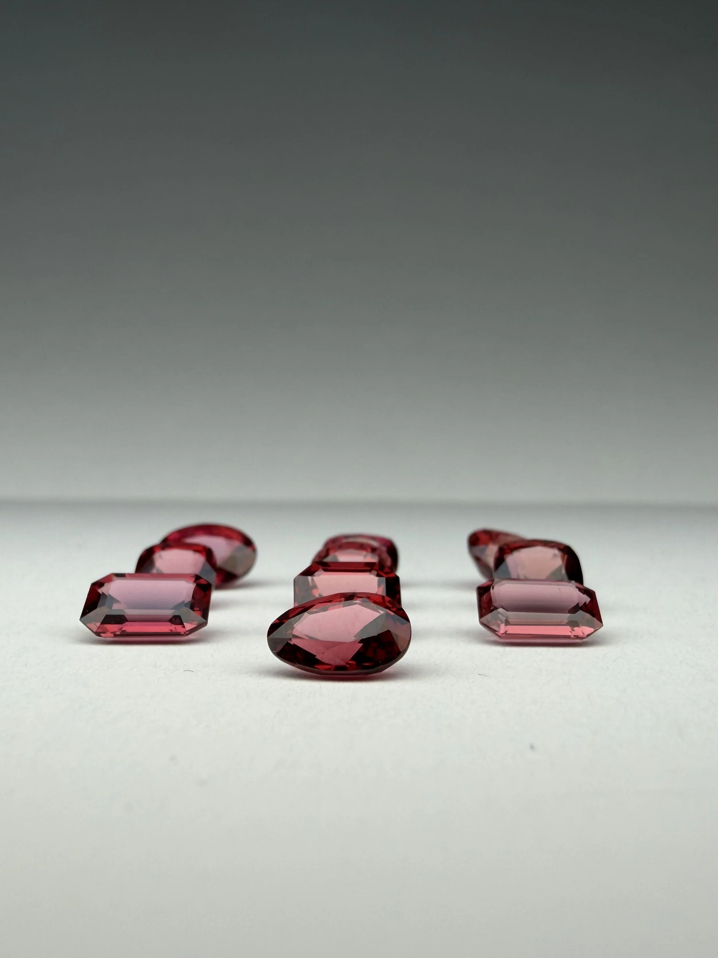 Gemmes rectangulaires et ovales en pierre précieuse rouge foncé disposées sur une surface blanche.