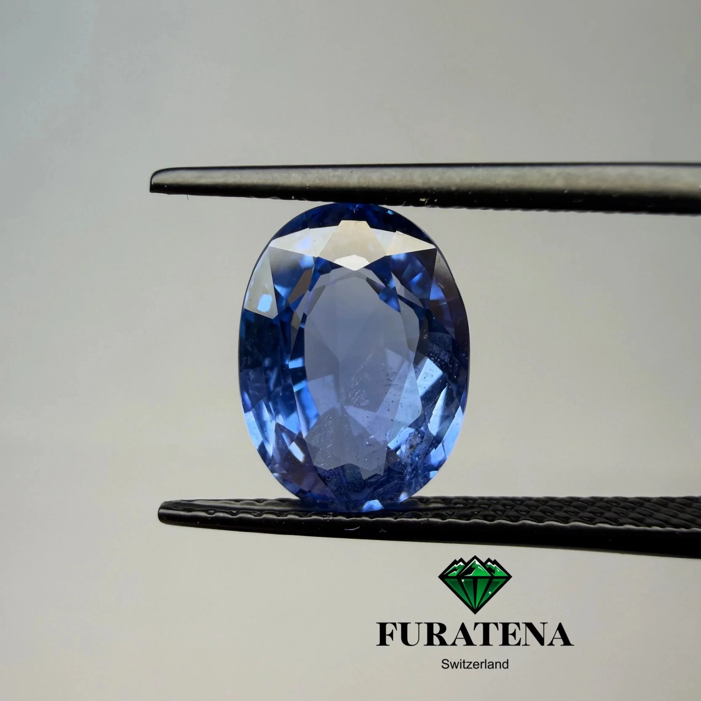 Une pierre précieuse bleu foncé est positionnée sous une pince à épiler noire. En dessous, le texte indique "FURATENA" avec une petite mention "Switzerland" en dessous, et un logo vert rappelant une montagne ou un diamant.