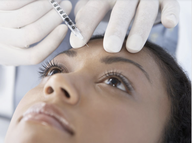 Close-up of woman receiving an injection between her eyebrows by someone wearing gloves.