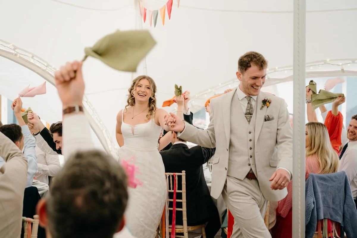 A wedding celebration with a bride and groom dancing, surrounded by guests at a decorated reception tent.