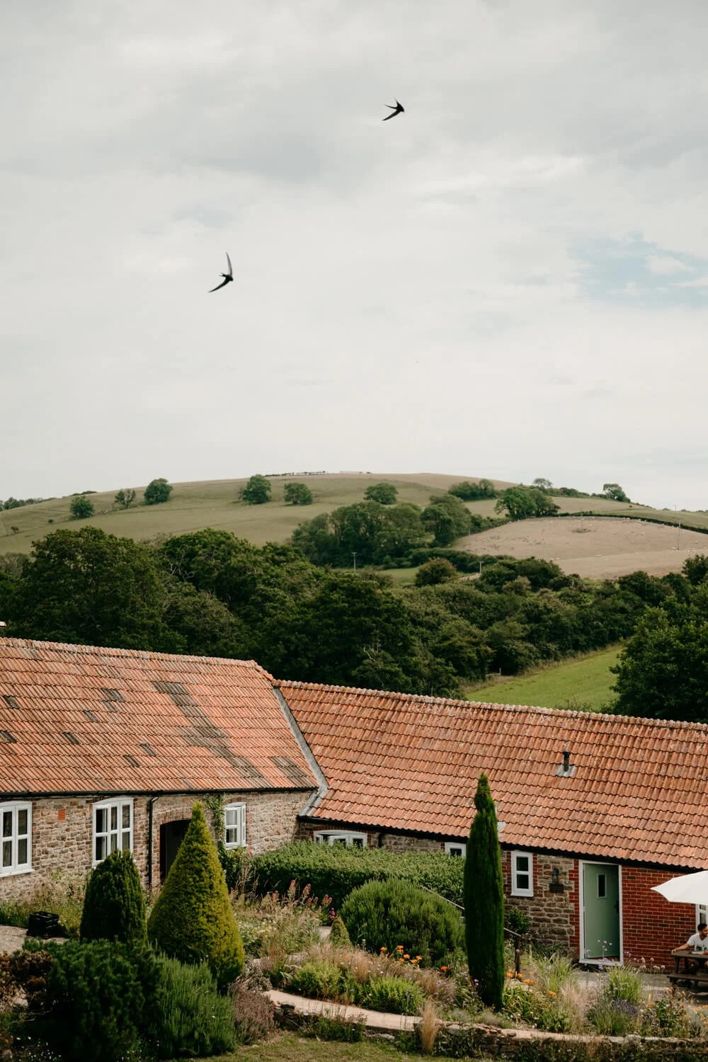 Photograph of the wedding venue Rudge Farm with birds flying over head with Dorset Countryside in the background