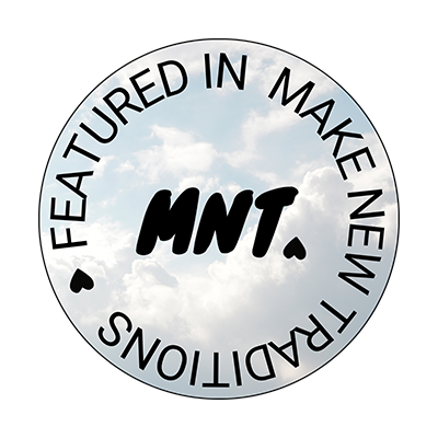 A circular badge with a sky and cloud background, featuring the text 'FEATURED IN MAKE NEW IDEAS' around the edges and 'MNT.' in bold in the center. Dorset Wedding Photographers, pip&clo featured in MNT