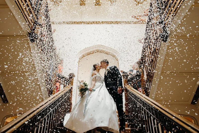 Bride and groom sharing a kiss at the top of a staircase at St Audries Park, Somerset during their wedding celebration with confetti photographed by Dorset wedding photographers pip&clo.