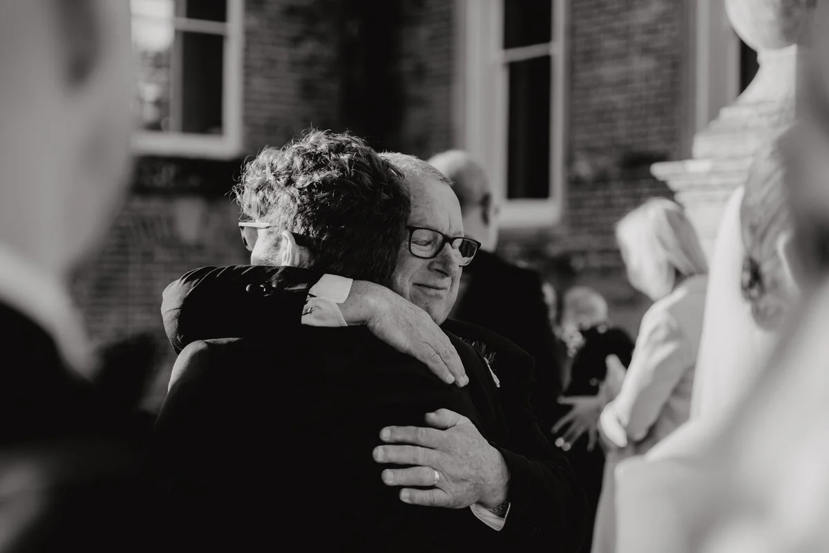 Two people hugging during a wedding, with others in the background, outside of Crowcombe Court, Somerset.