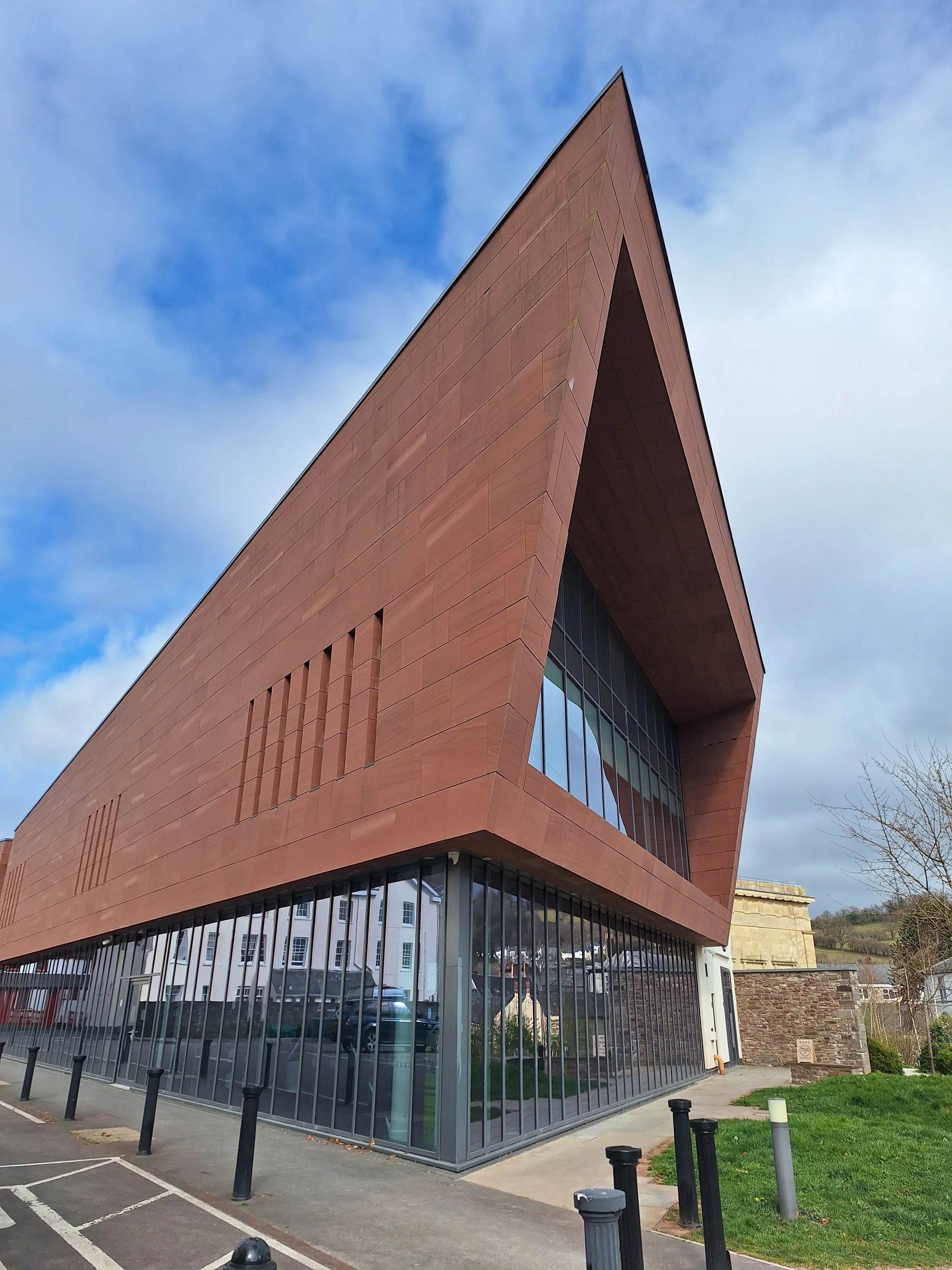 Modern building with sharp angles, red exterior, large glass windows, and a parking lot in front.