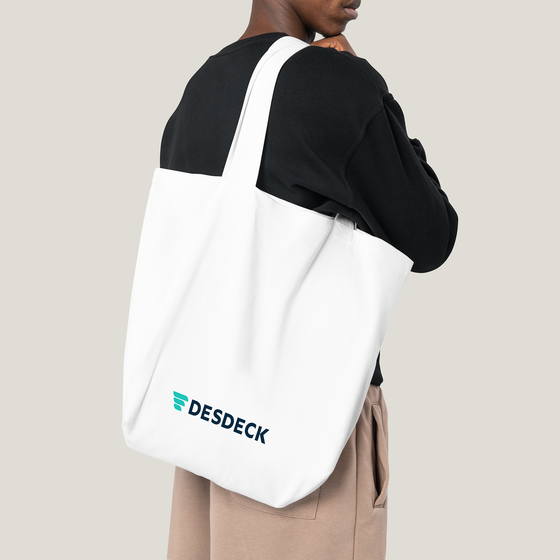 Person carrying a white tote bag with the 'DESDECK' logo against a neutral background.
