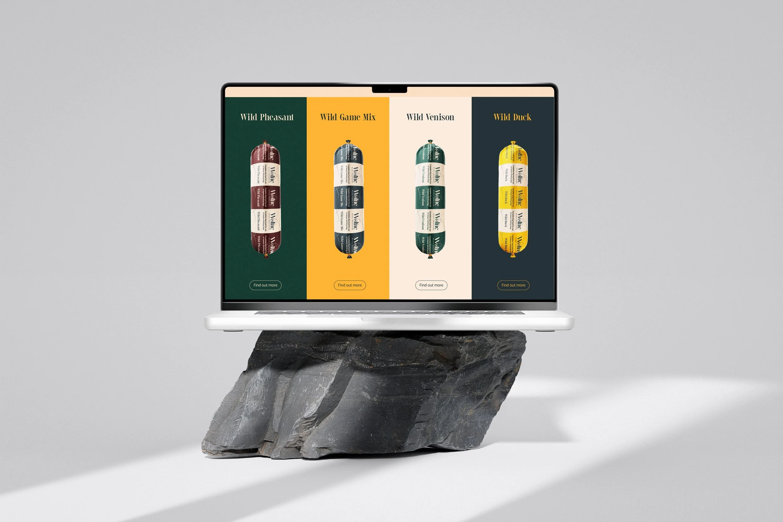 Laptop displaying four color-varied packaged products labeled Wild Pheasant, Wild Game Mix, Wild Venison, and Wild Duck, on a piece of dark, rough stone against a plain light gray background.