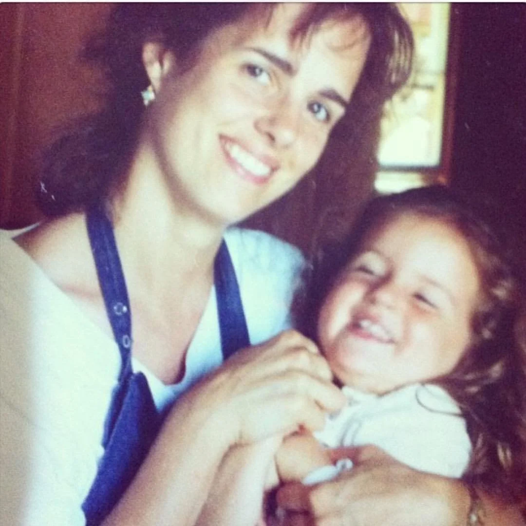 A woman and a young girl smiling and holding hands.