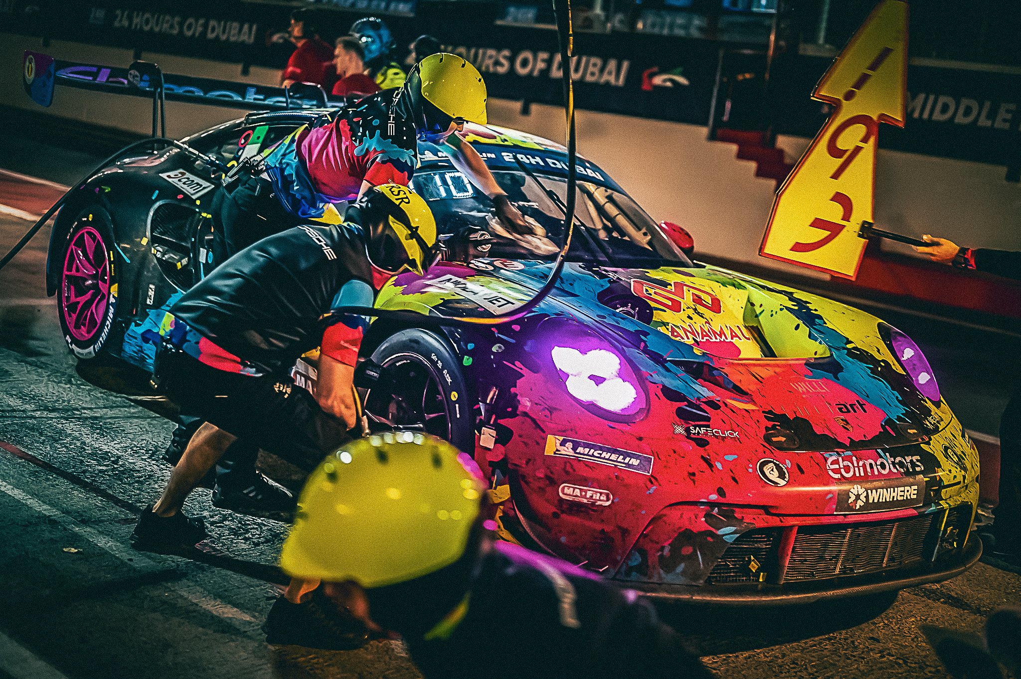 Echipa Willi Motorsport în timpul unui pit-stop de noapte la 24H Dubai, lucrând sincronizat pe un Porsche GT3 colorat distinctiv în timpul unei curse de anduranță.