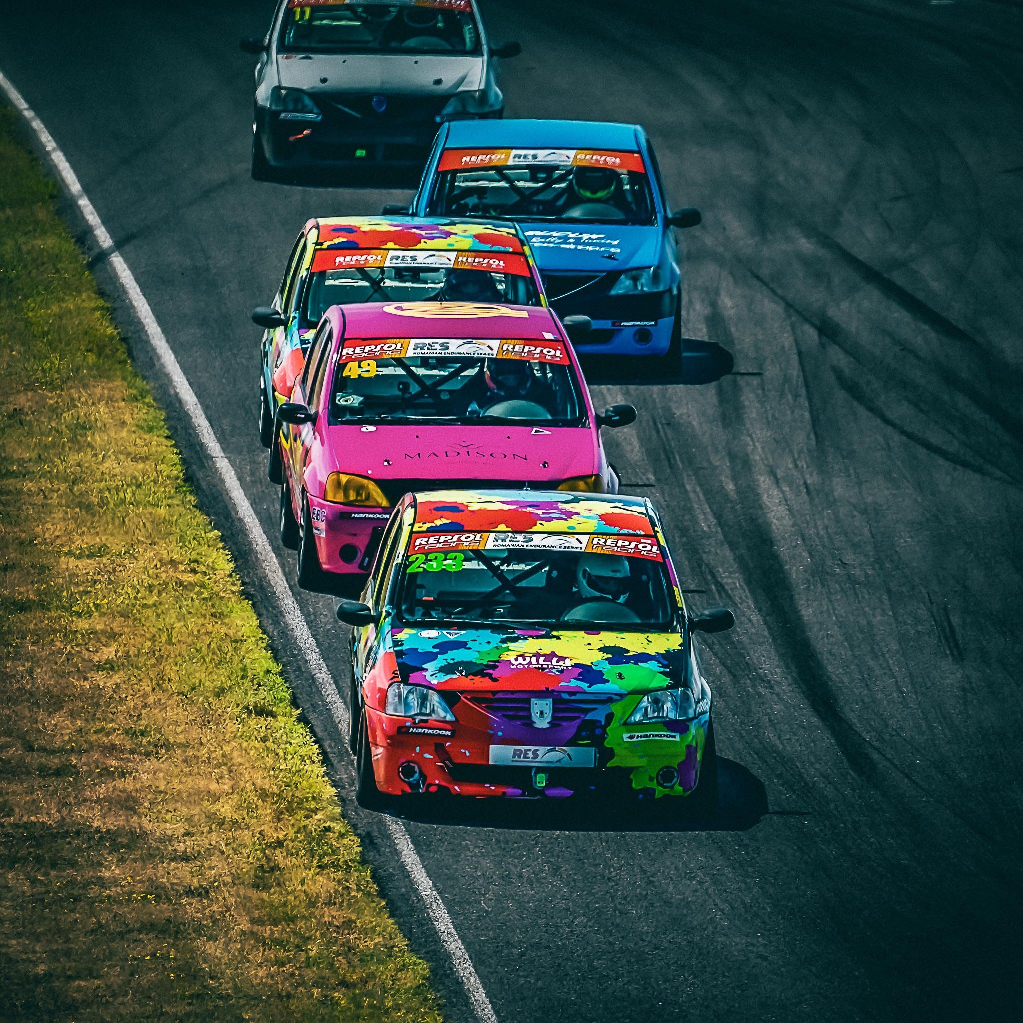 David Nicolaie la volanul mașinii #233, conducând plutonul într-un viraj strâns din cadrul Logan Cup – Romanian Endurance Series. Mașini colorate strâns aliniate pe circuit.