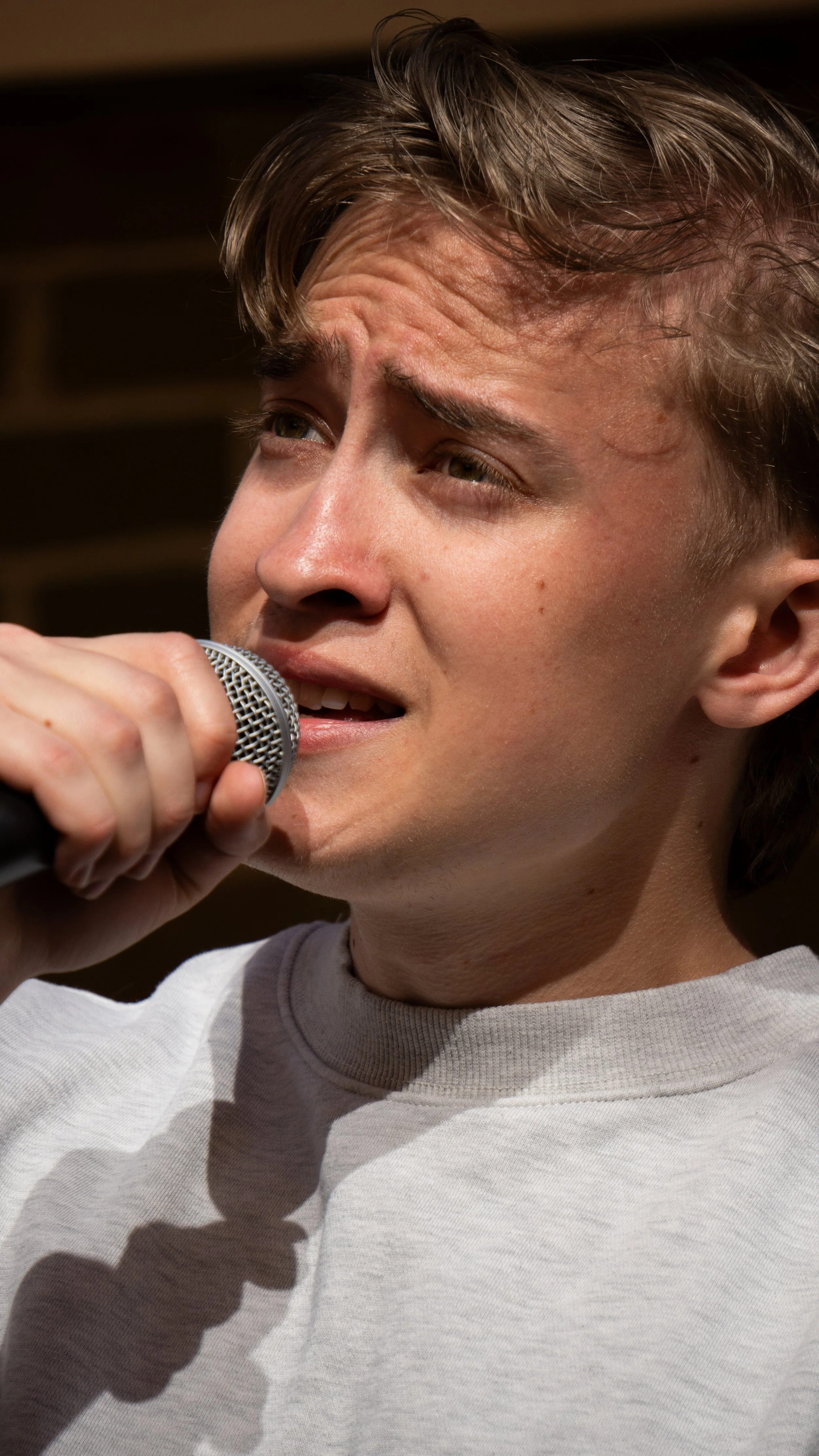 Young man singing into a microphone with an emotional expression.