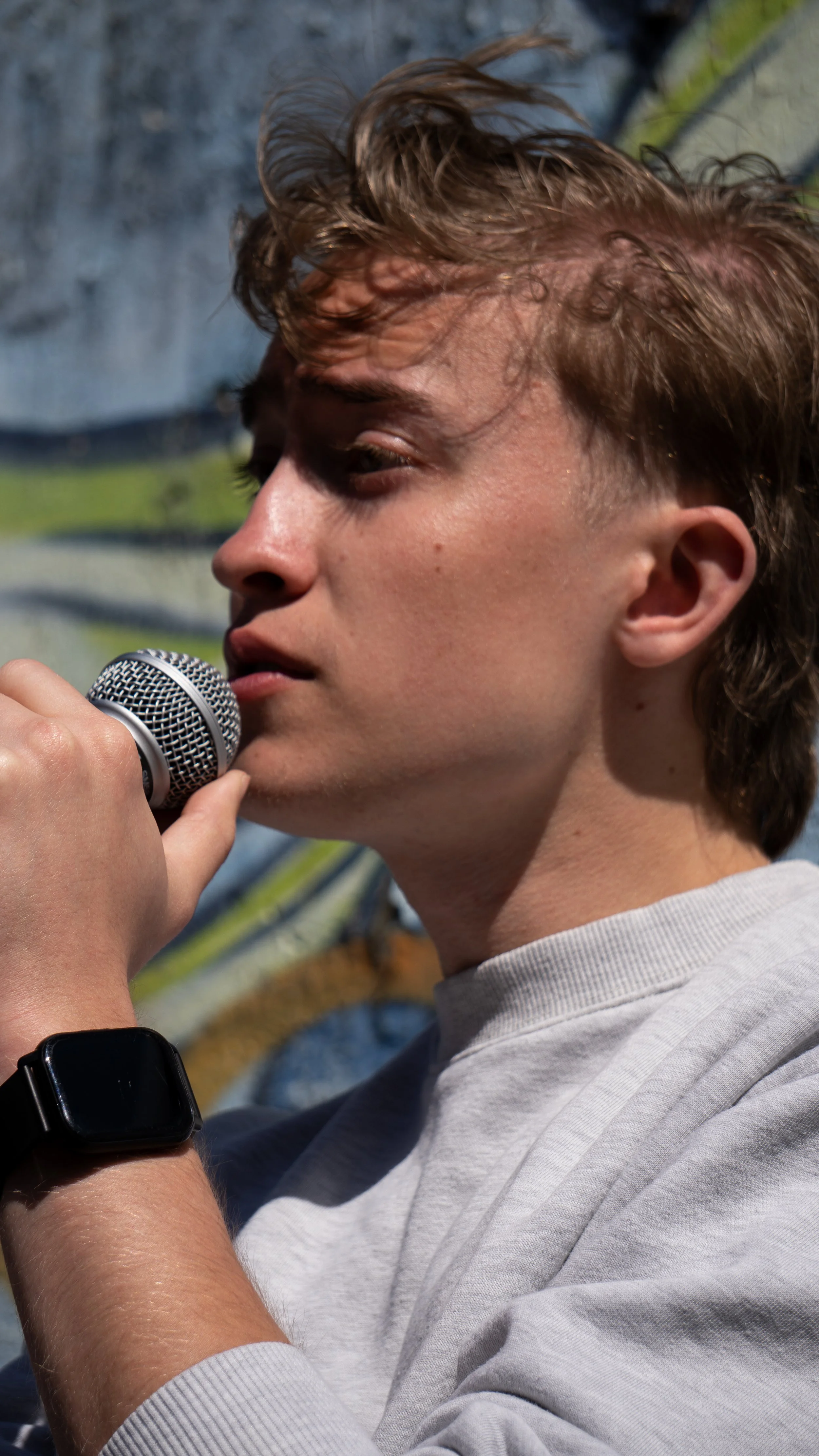 Young man holding a microphone with a scenic outdoor background.