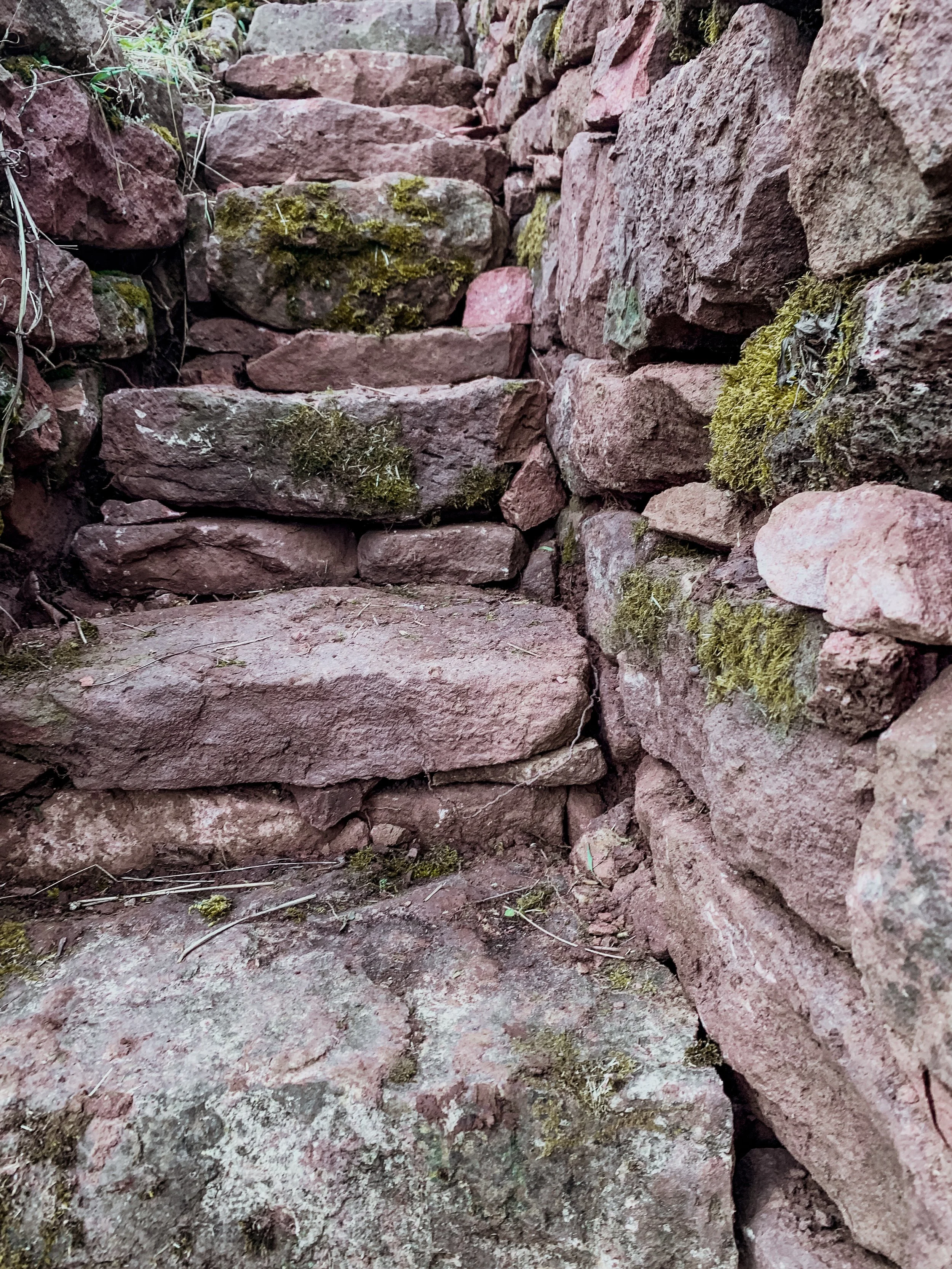 Ein steiler Weg aus roten Steinen, umgeben von Mauern aus gleichen Steinen, mit Moos bewachsen.