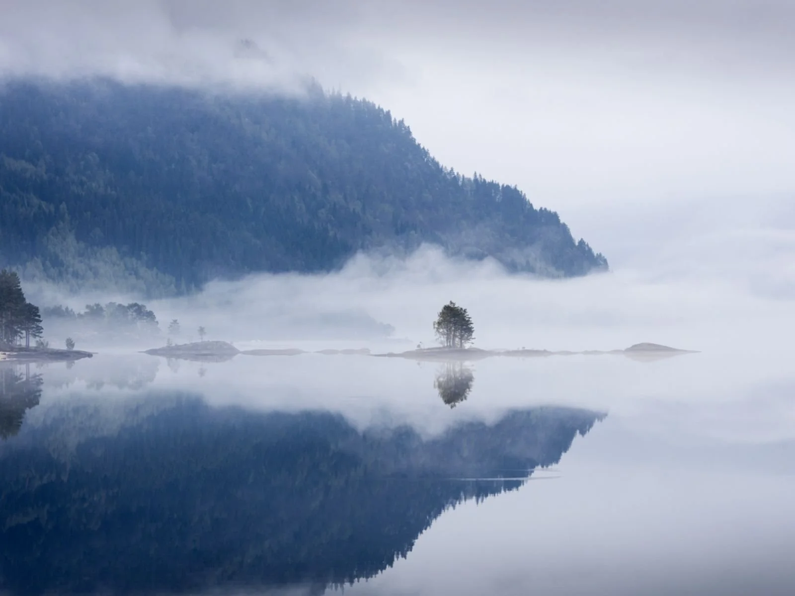 Fjell omgitt av tåke og refleksjon i vann