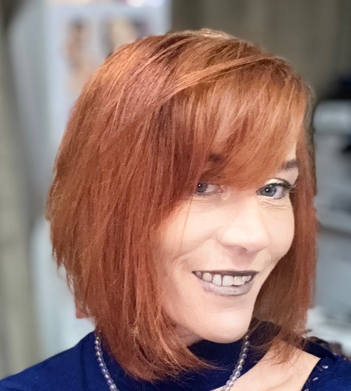 Une femme avec des cheveux roux, portant un collier, souriant.