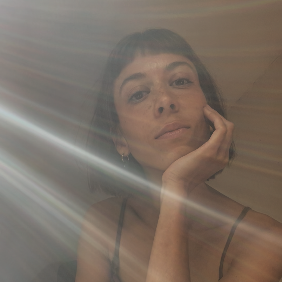 Porträt einer Frau, die in die Kamera schaut, mit dunklen Haaren und einem dunklen Oberteil, durch eine durchscheinende Oberfläche fotografiert, Lichtstrahlen reflektieren.