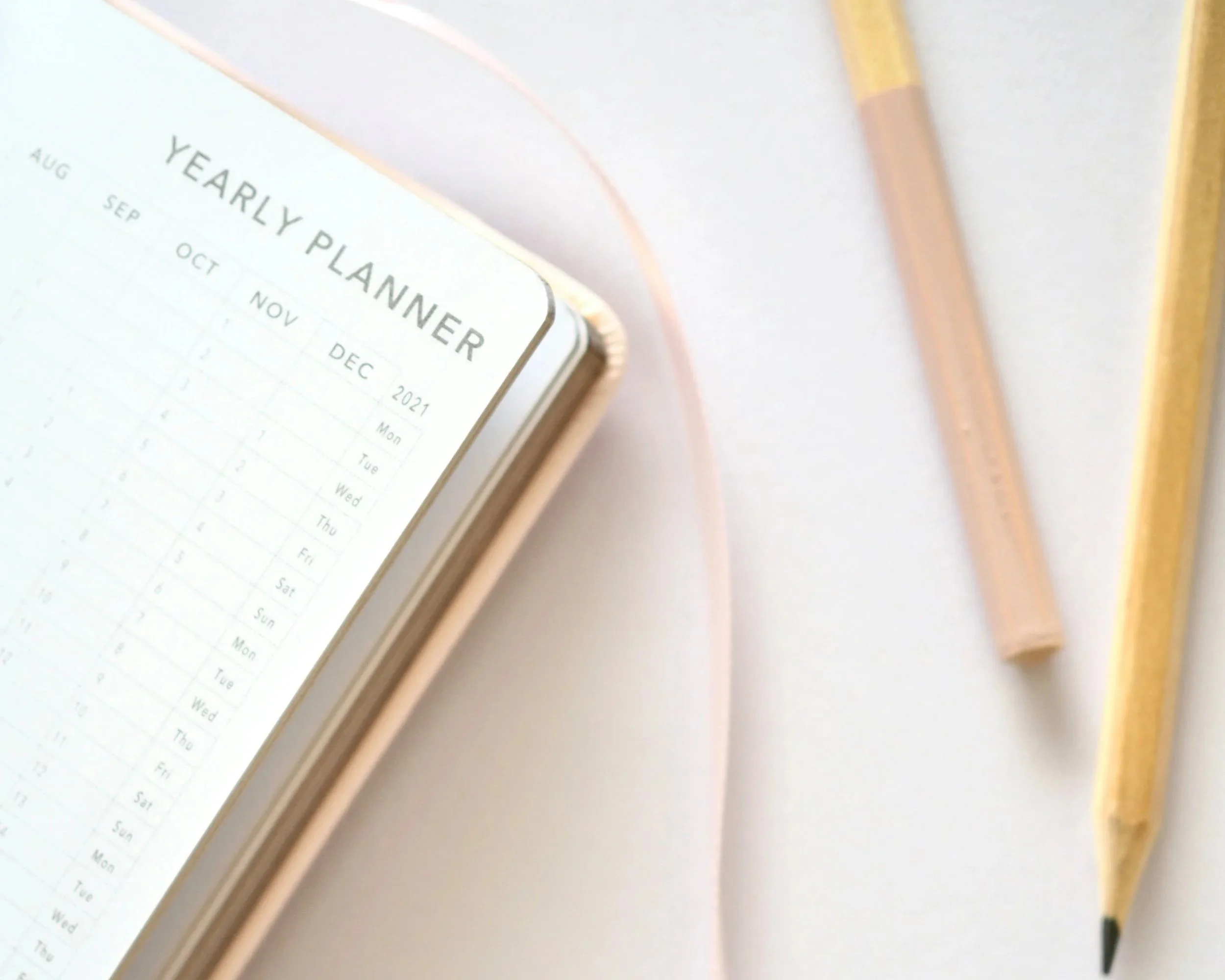 Open planner with monthly calendar pages for September to December 2021, labeled "Yearly Planner". Two pencils, one pink and one yellow, are beside the planner on a white surface.
