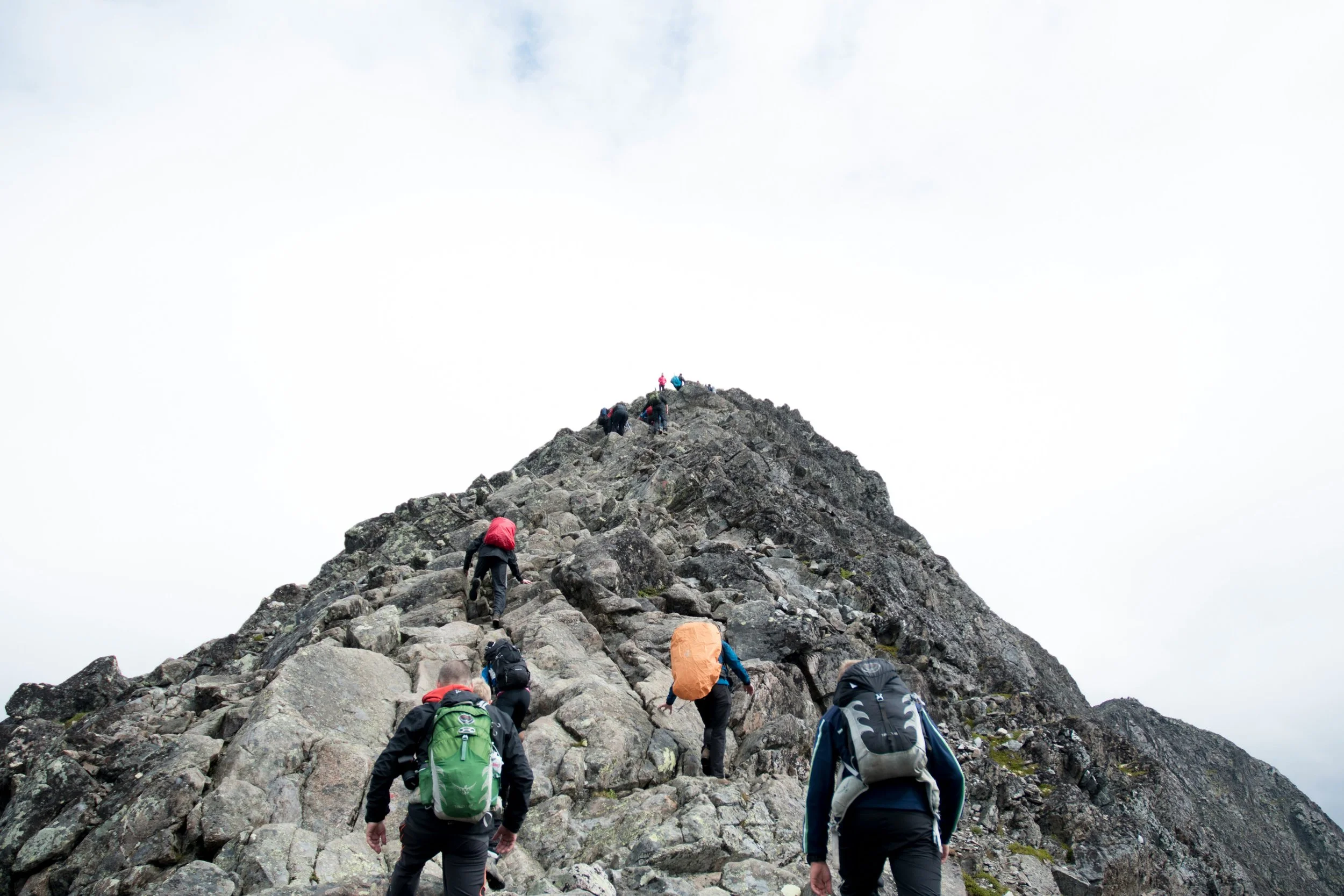 Group of hikers climbing a steep, rocky mountain trail under cloudy sky.