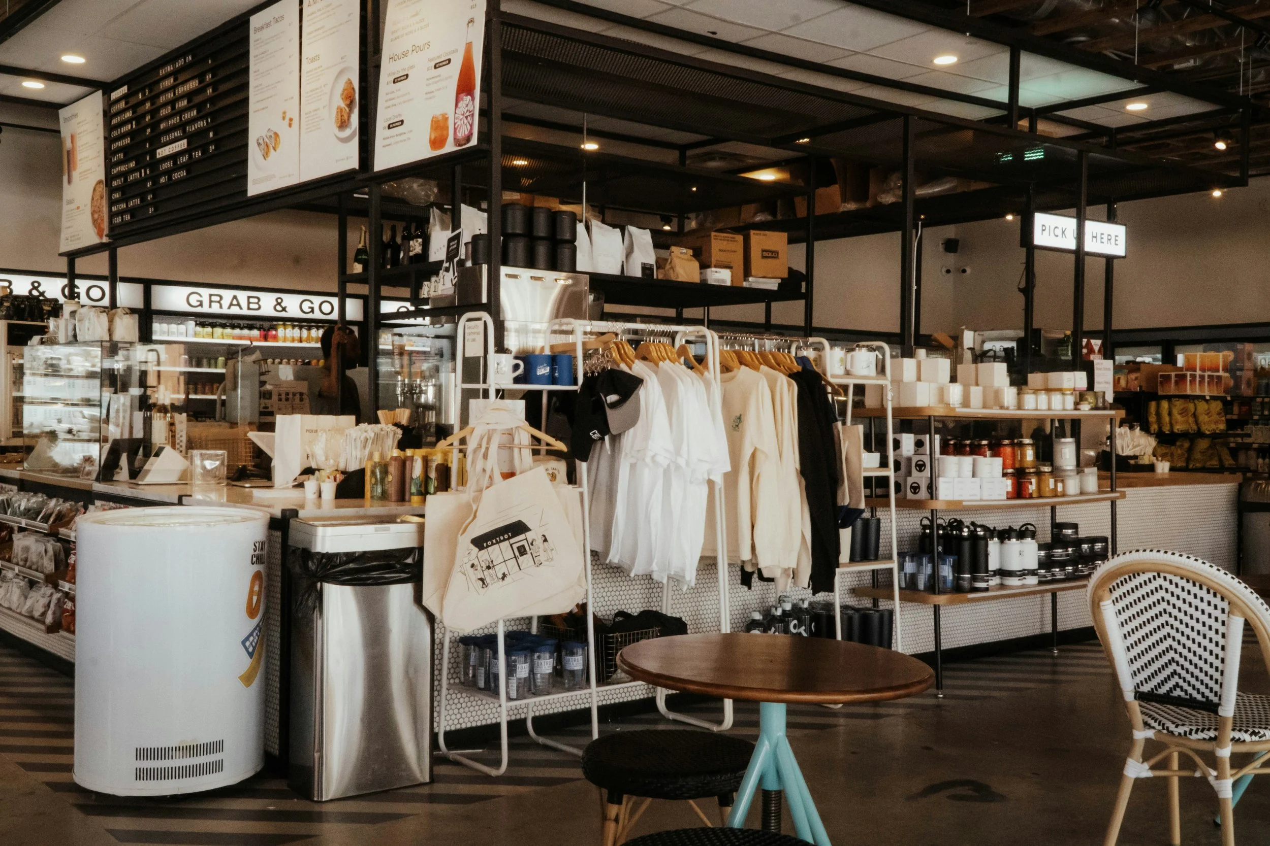 Interior of a coffee shop with merchandise on display, including clothing, mugs, and accessories, with a menu board hanging above.