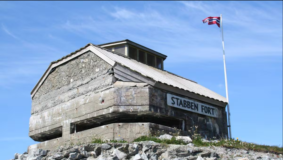 En gammel festning med skiltet "Stabben Fort", et norsk flagg og en blå himmel med noen skyer.