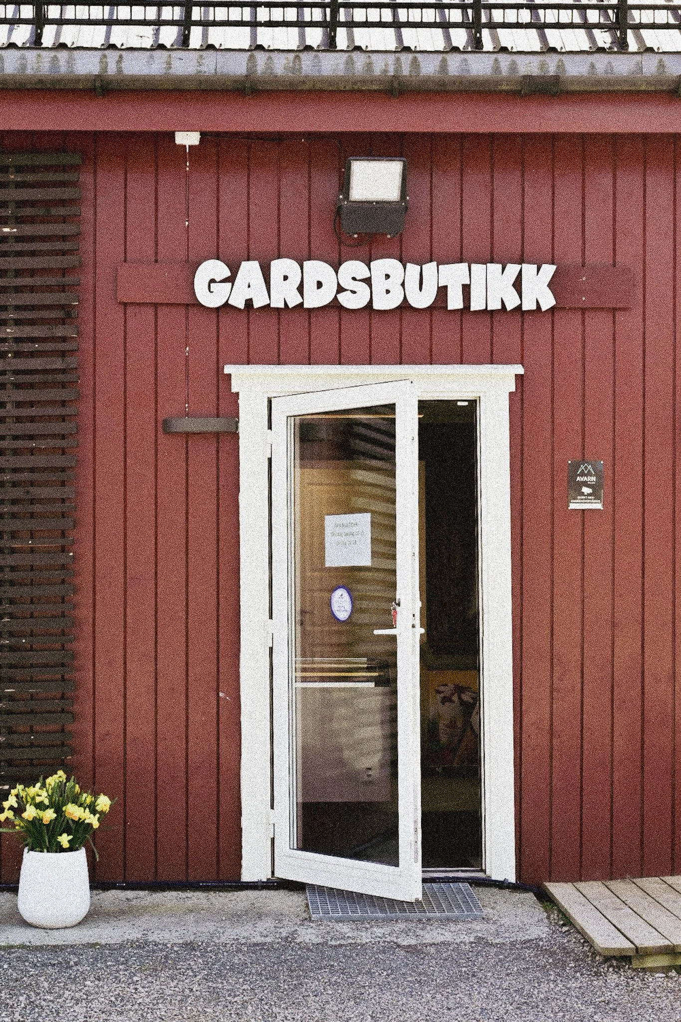 En rød vegg med glassdør og et skilt med Gardsbutikk