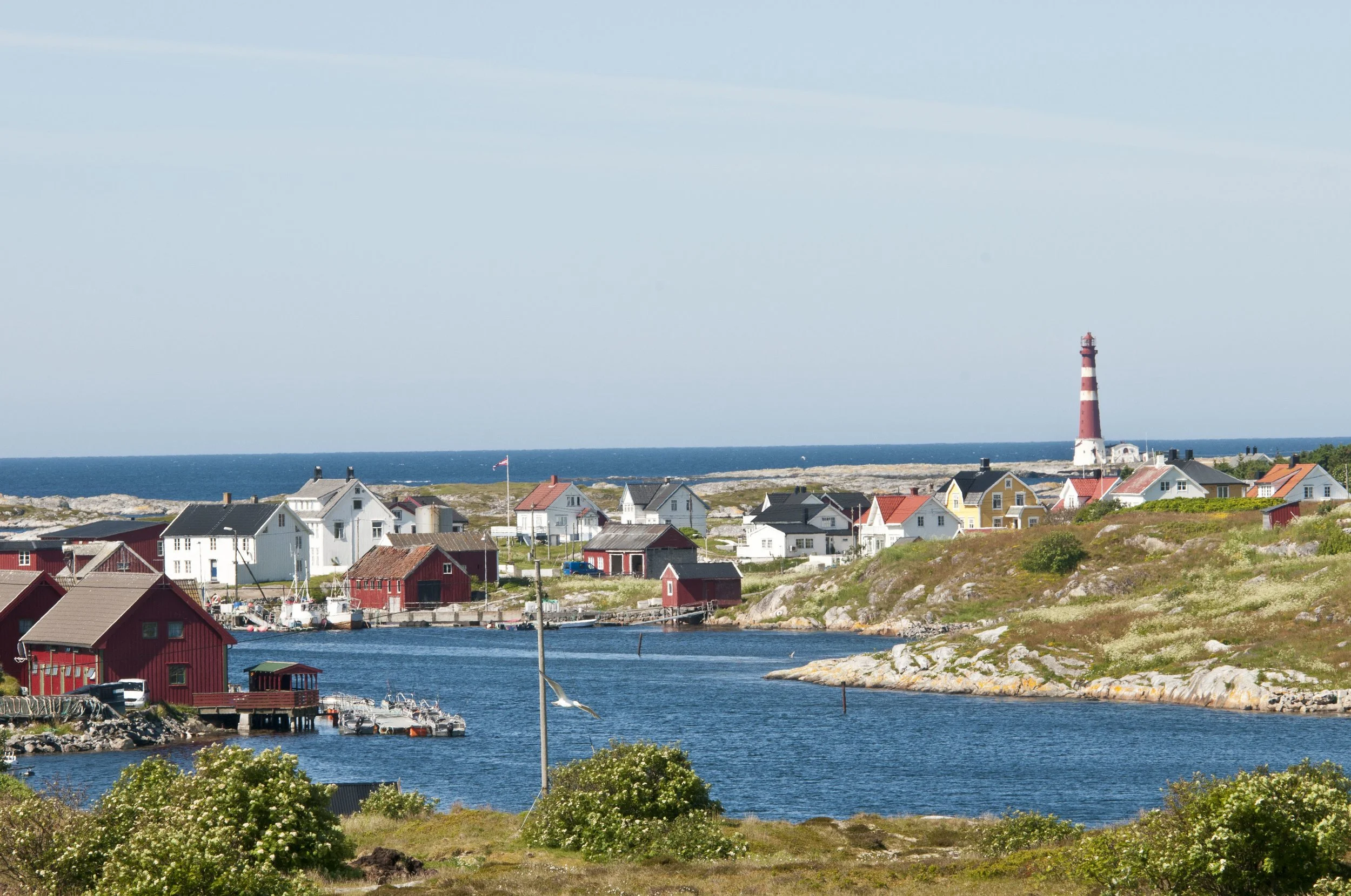 Landskapsfoto av Titran på en solfylt dag. Sletringen Fyr synes lengst bort til høyre, omringet av kysthus.