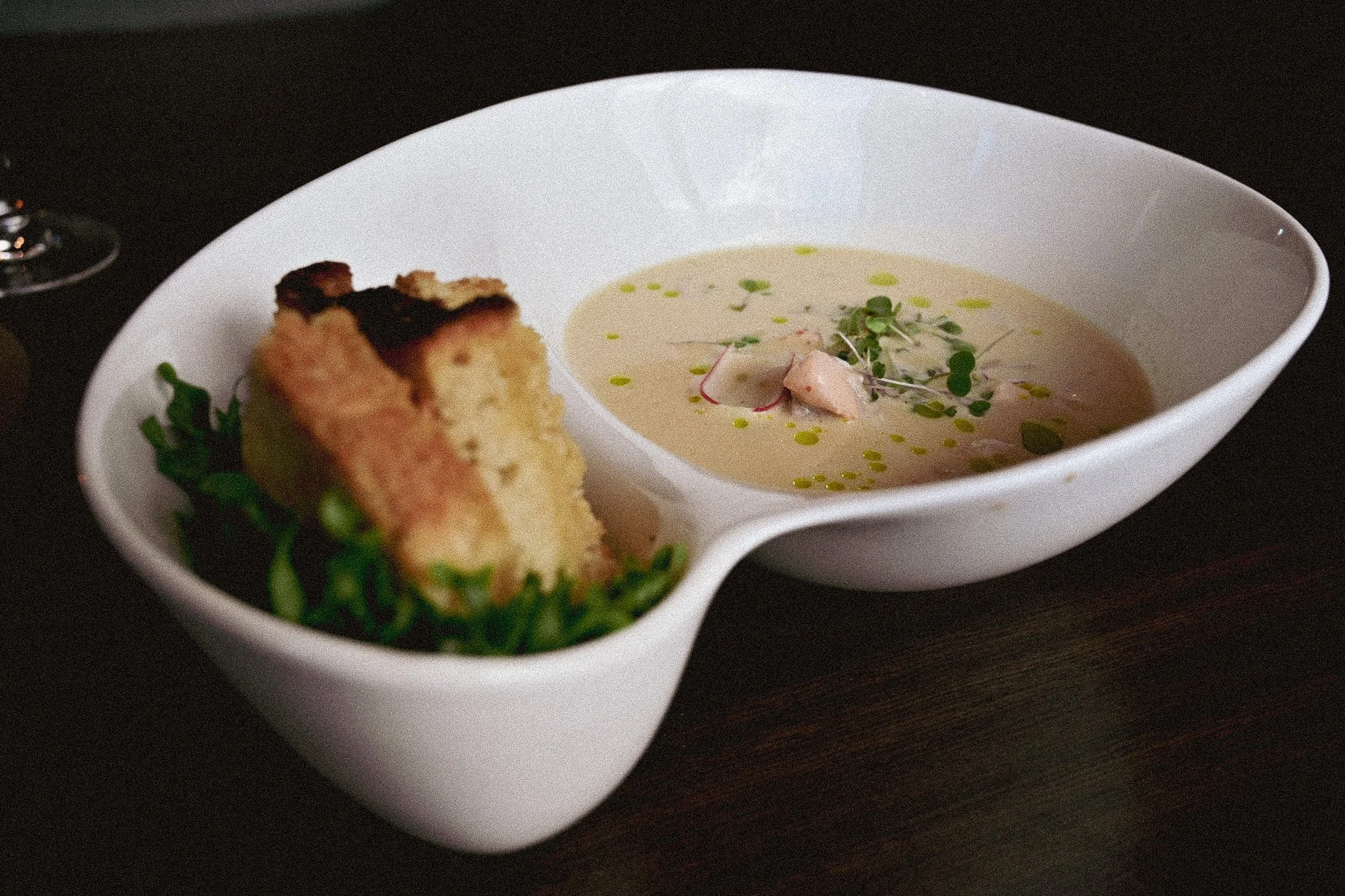 En tallerken med fiskesuppe i hvit skål og en brødskive med smør, pyntet med urter på et mørkt bord.