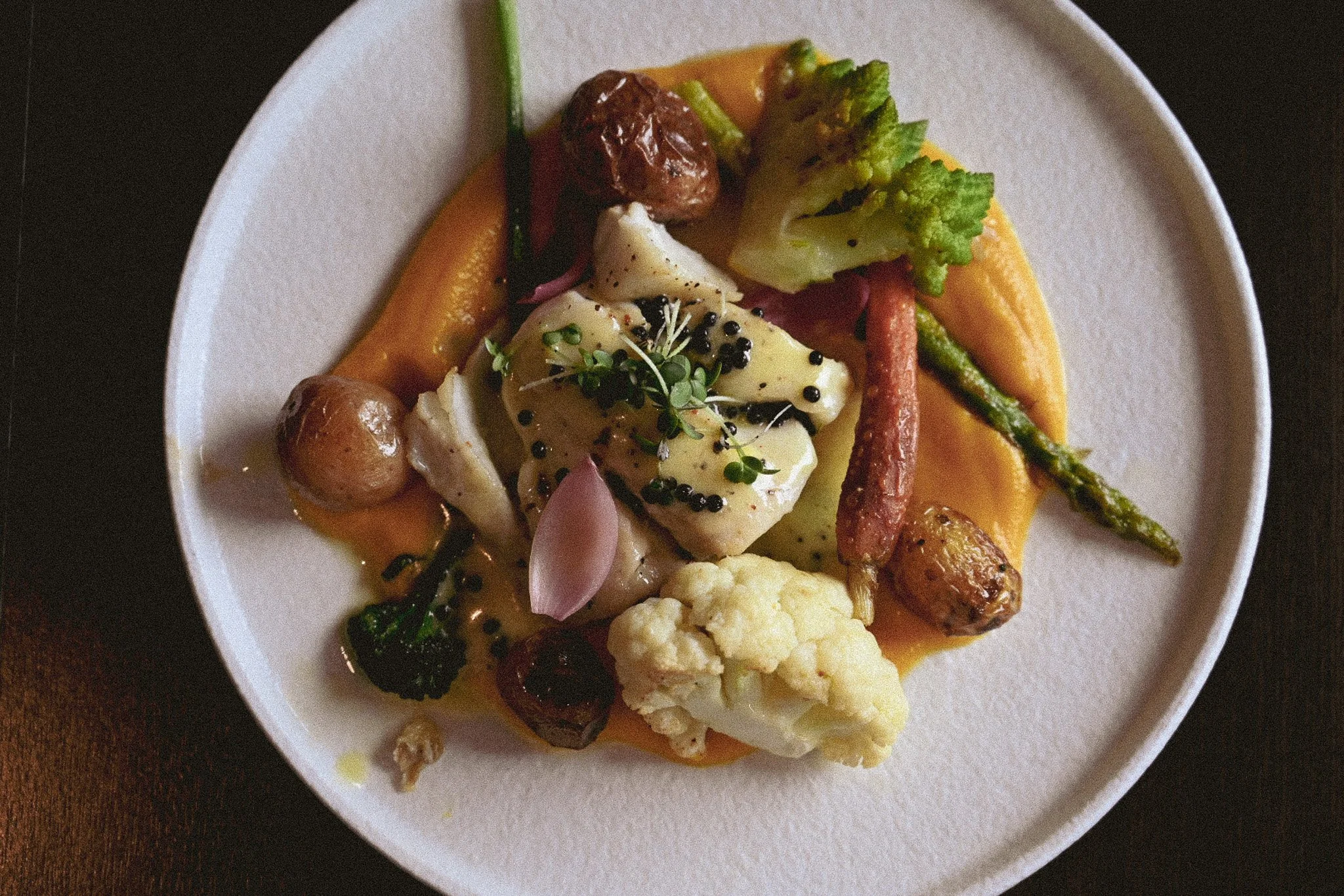 Hvit tallerken på sort bord med fisk, gulerotpurè og grønnsaker