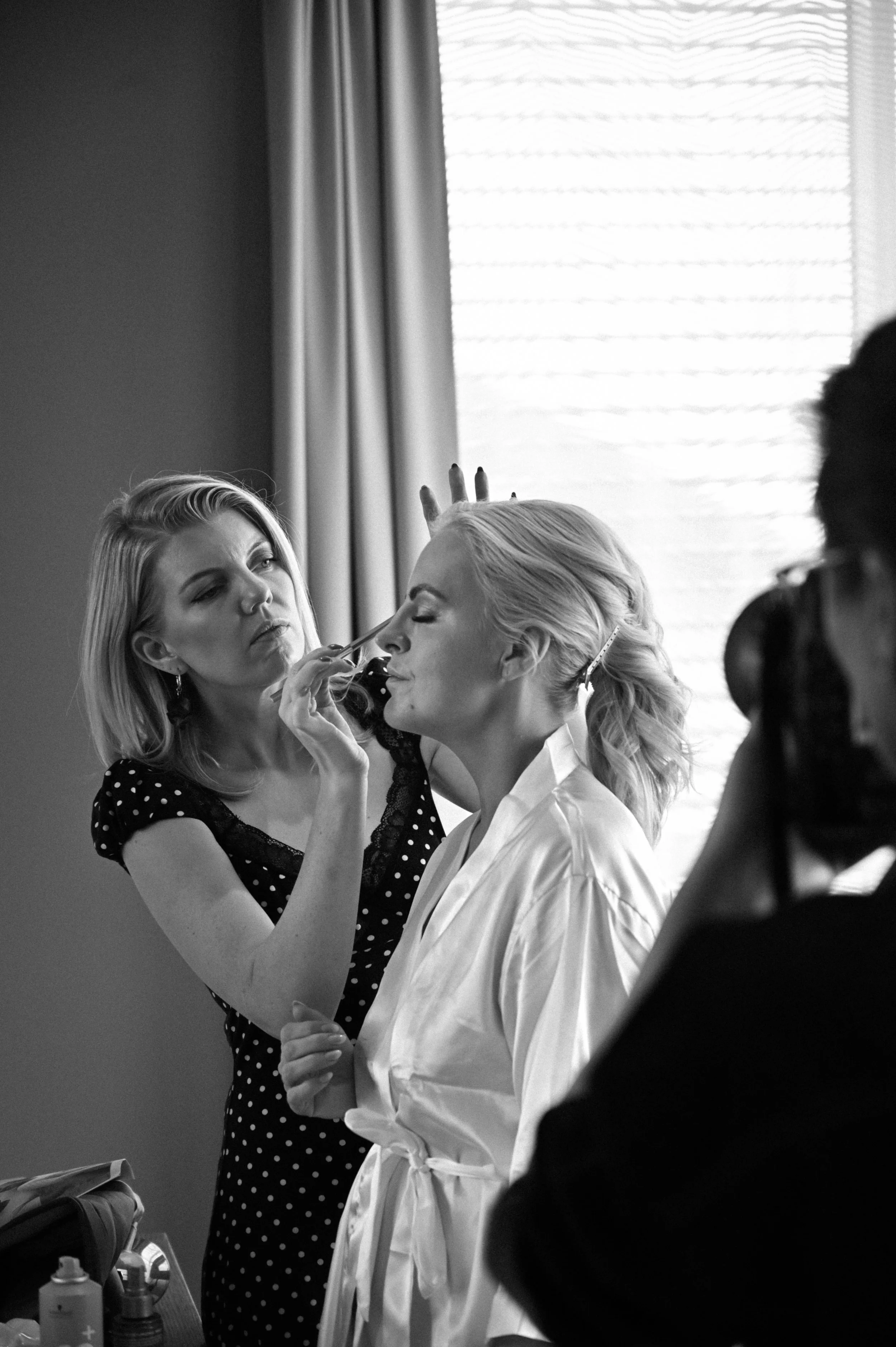 En makeup-artist sminker en kvinnes ansikt med sminke i en hotellsuite.