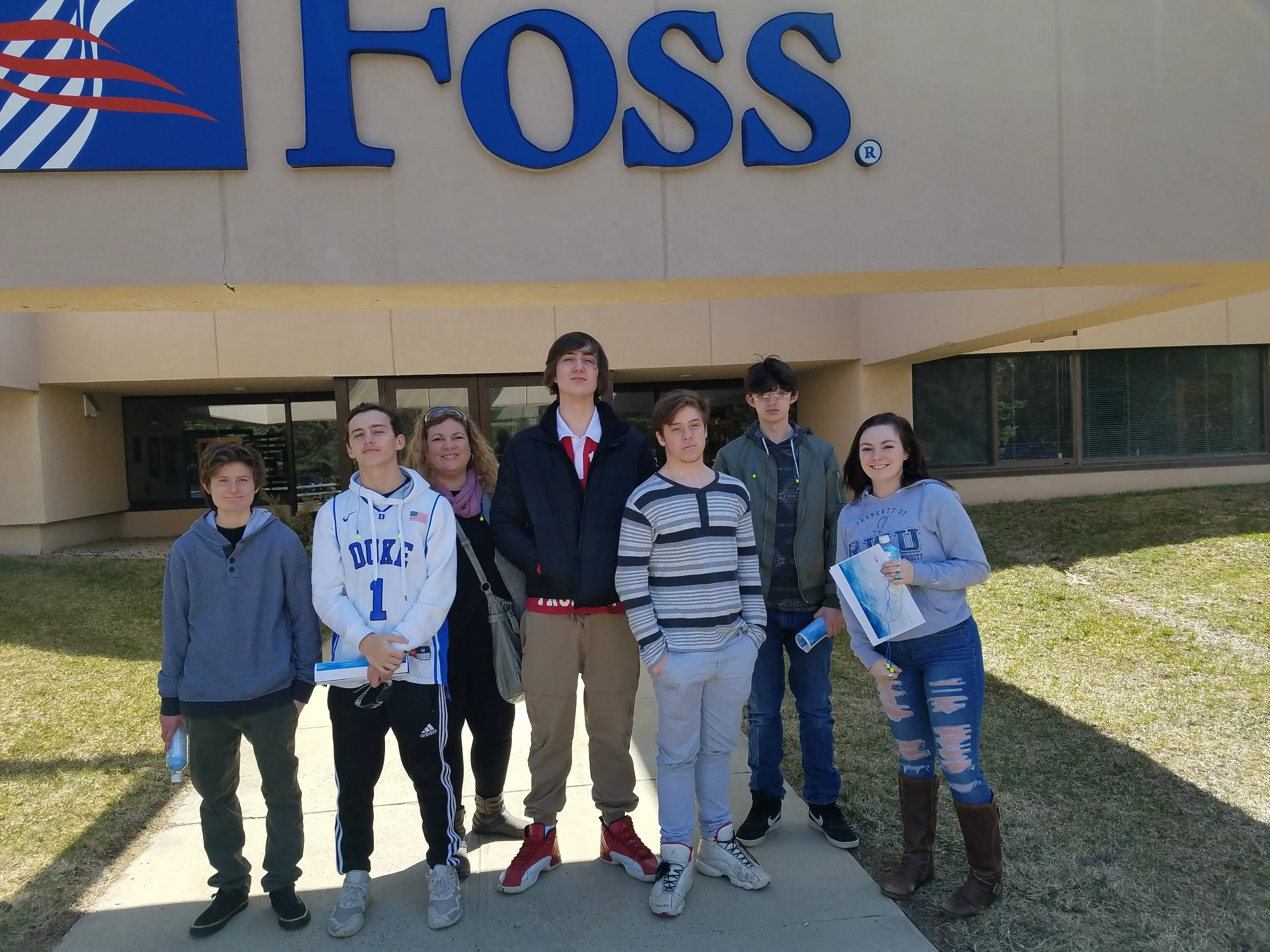Group of seven young people standing outside in front of a building with a large