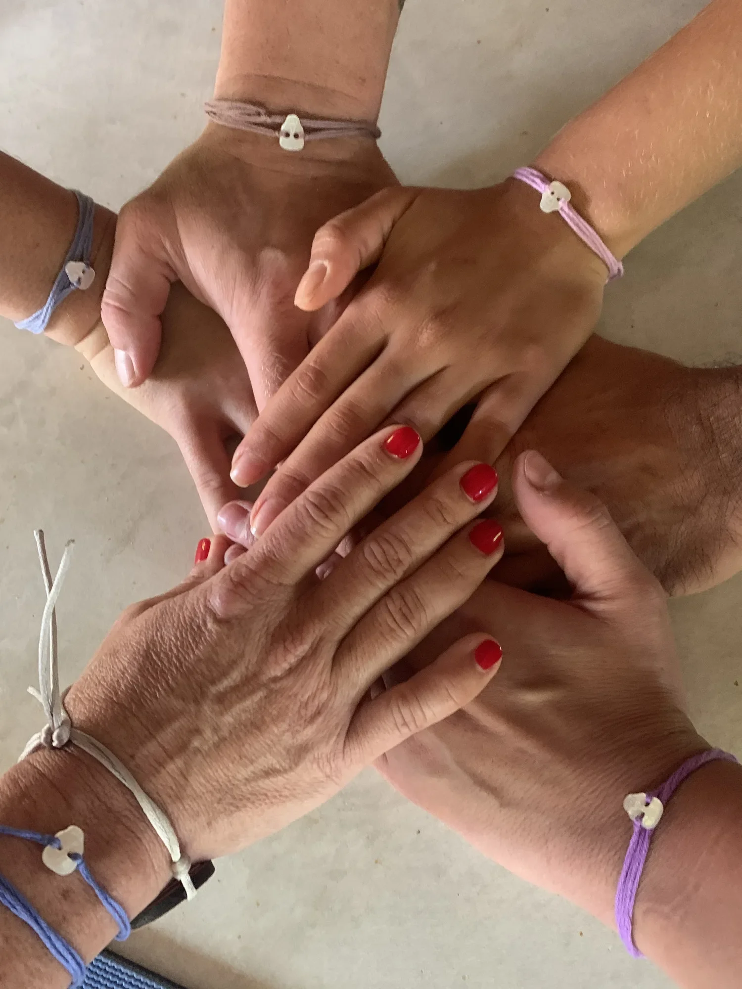 Four hands stacked on a table, each wearing a matching friendship bracelet.