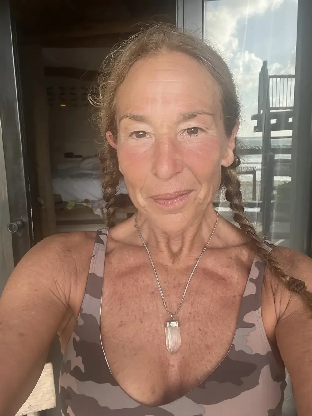 Halle in the doorway of the house in Tulum, braids and a quartz pendant, the balcony and the ocean behind her.