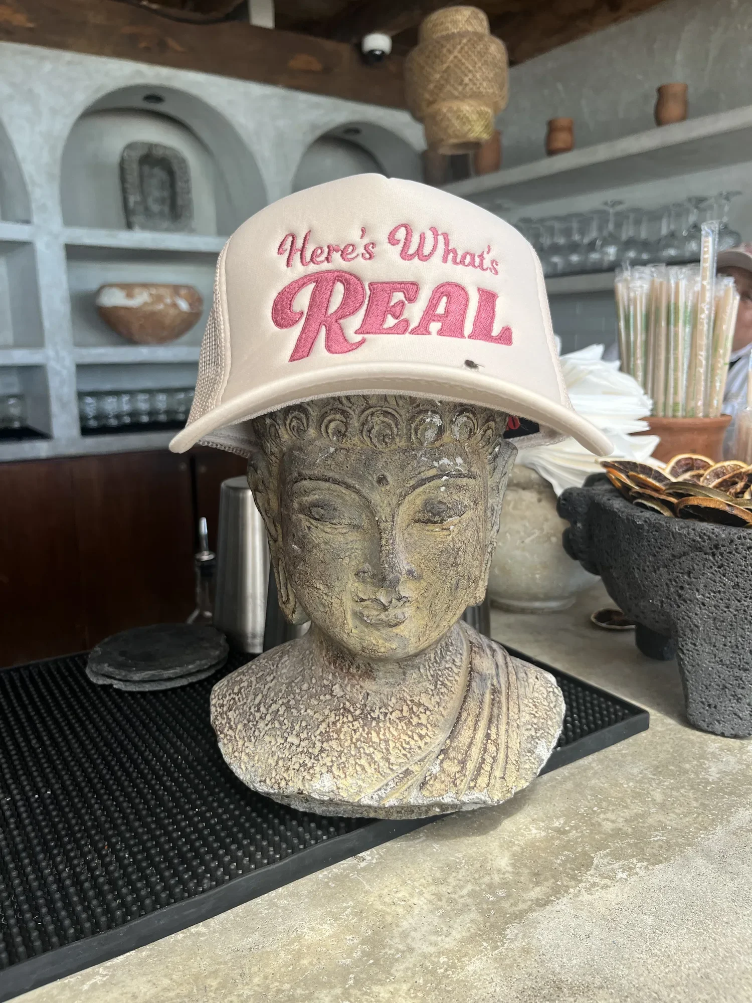 A stone Buddha head on the bar wearing one of the retreat trucker hats.