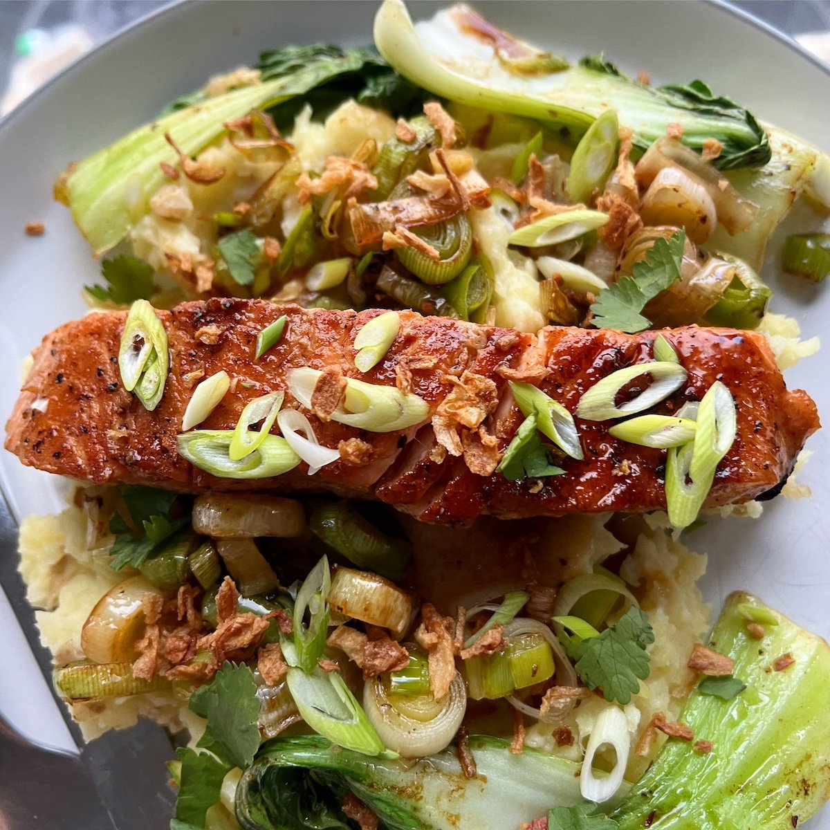 Grilled salmon topped with sliced green onions and crispy fried onions, served with sautéed greens and mashed potatoes.